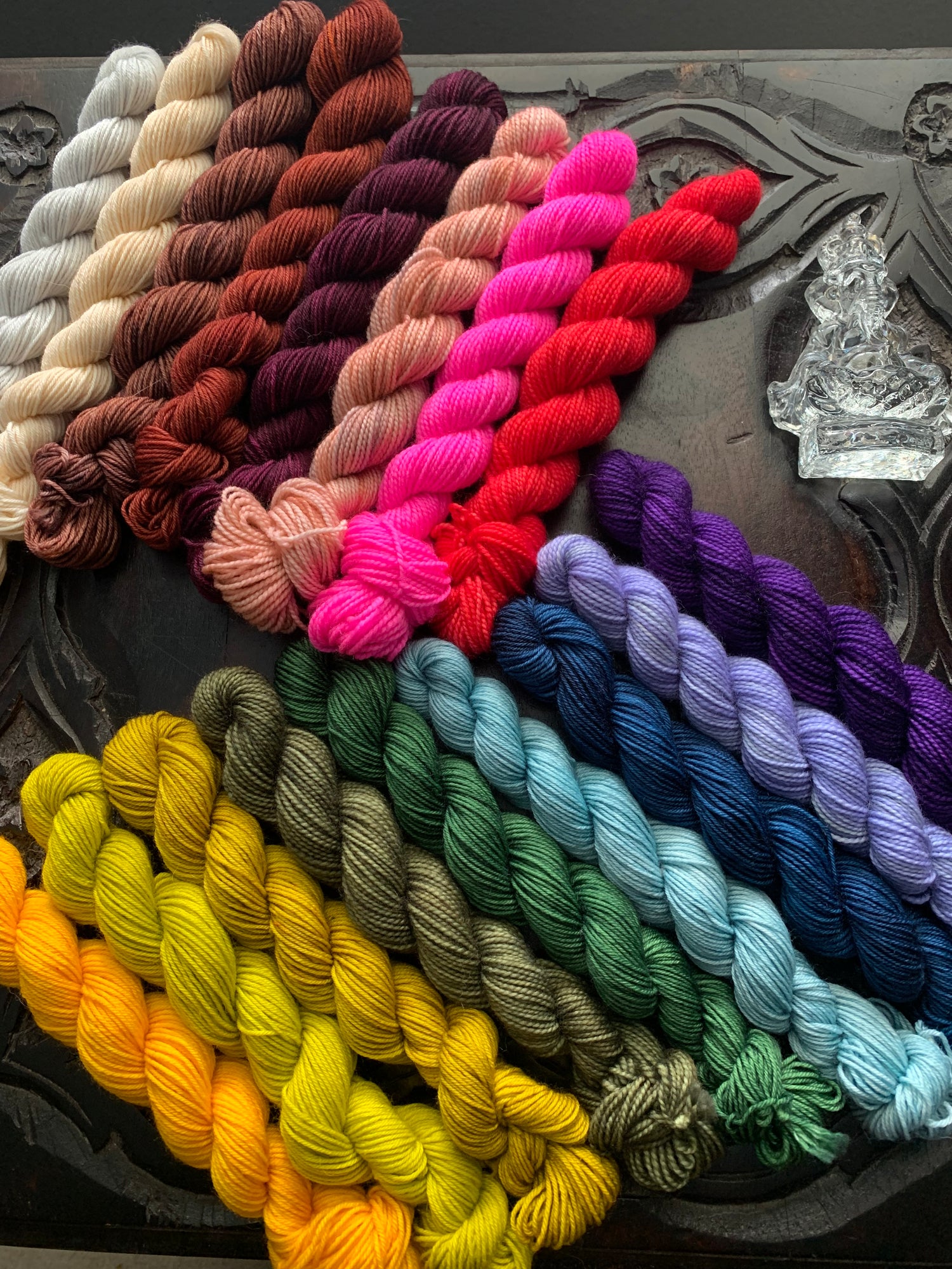 Minis skeins in off-white, cream, brown, peach, bright pink, red, yellows, greens, blues and purples, lay on a table.
